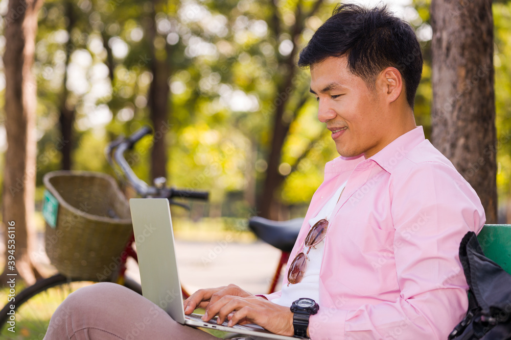 Asian man sitting at work on a laptop in a park. Asian man sitting at work on a laptop in a park.