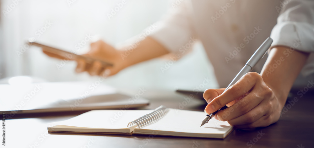 Hand of a business woman with a pen and a smartphone working on documents on the table in office.