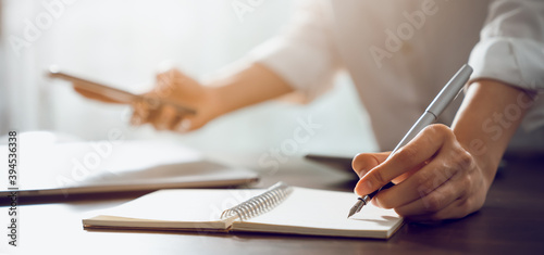 Hand of a business woman with a pen and a smartphone working on documents on the table in office.
