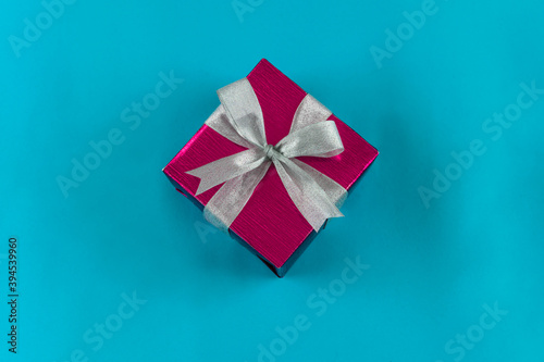 Top view of gift box wrapped in red paper with ribbon on blue colour background. Copy space for text. Holiday concept. Time gifts.