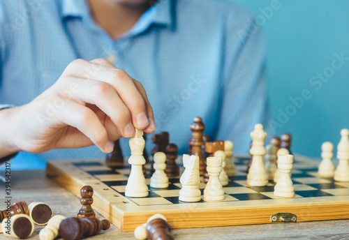 Teenager plays chess. Boy makes move with a figure on wooden chessboard. Hobby, leisure concept