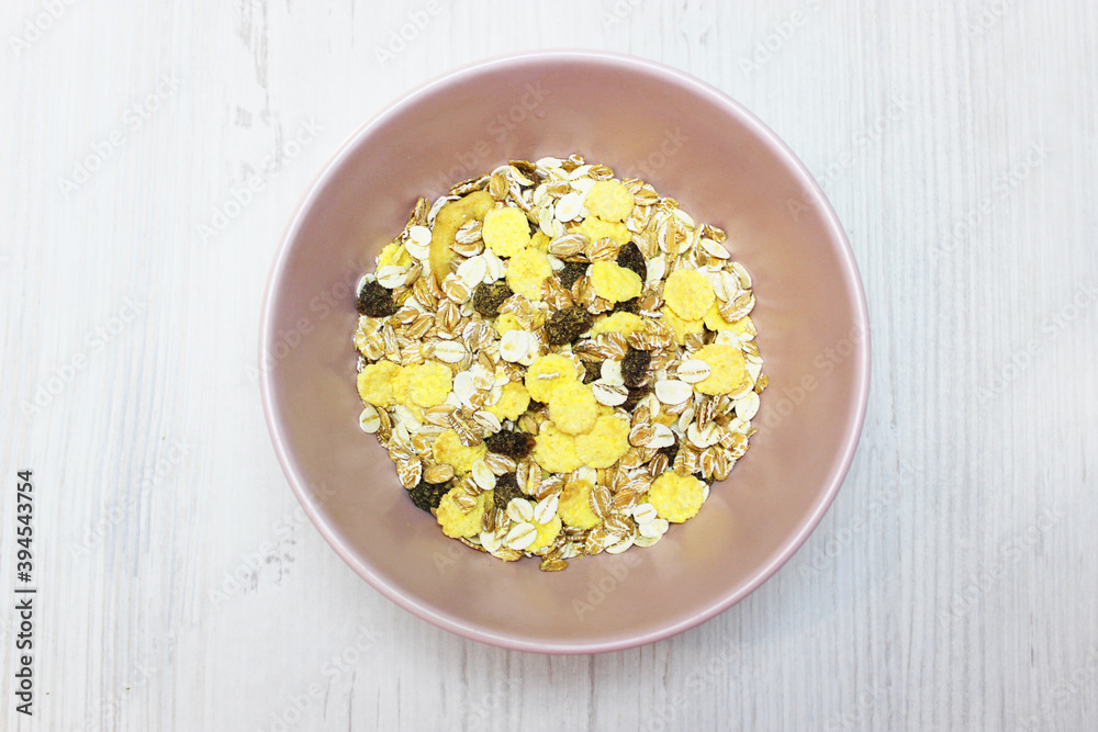 muesli with on a pink plate, top view. Muesli with fresh milk, yogurt or kefir. Muesli is made from oatmeal, a mixture of multi-grain flakes with dried fruits, nuts and sunflower seeds. on a white muesli with on a pink plate, top view. Muesli with fresh milk, yogurt or kefir. Muesli is made from oatmeal, a mixture of multi-grain flakes with dried fruits, nuts and sunflower seeds. on a white