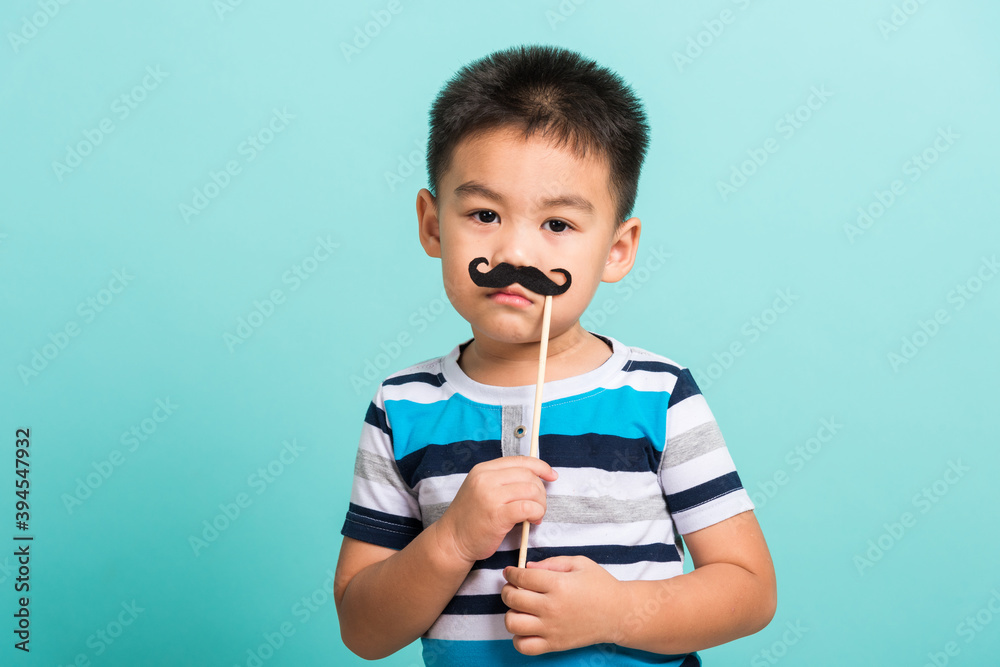 Funny happy hipster kid holding black mustache props for the photo booth close face, studio shot isolated on a blue background, Men health awareness, Prostate Cancer Awareness Funny happy hipster kid holding black mustache props for the photo booth close face, studio shot isolated on a blue background, Men health awareness, Prostate Cancer Awareness