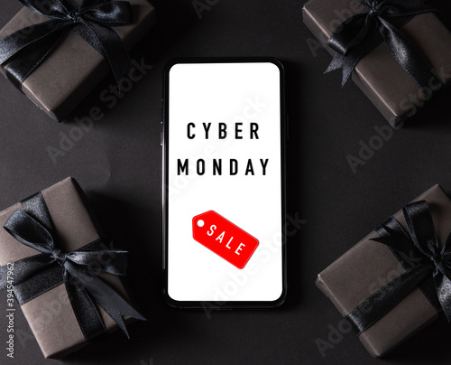 Cyber Monday sale shopping concept, Top view of gift box wrapped black paper and black bow ribbon present around smartphone blank screen, studio shot on dark background photo