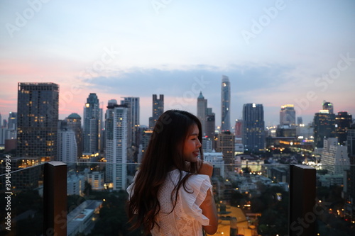 Asian Girl in white dress standing on the roof top bar with good top building in downtown view. City scape concept 