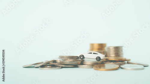 white miniature car on pile of coins with blue-green background , business and finance background