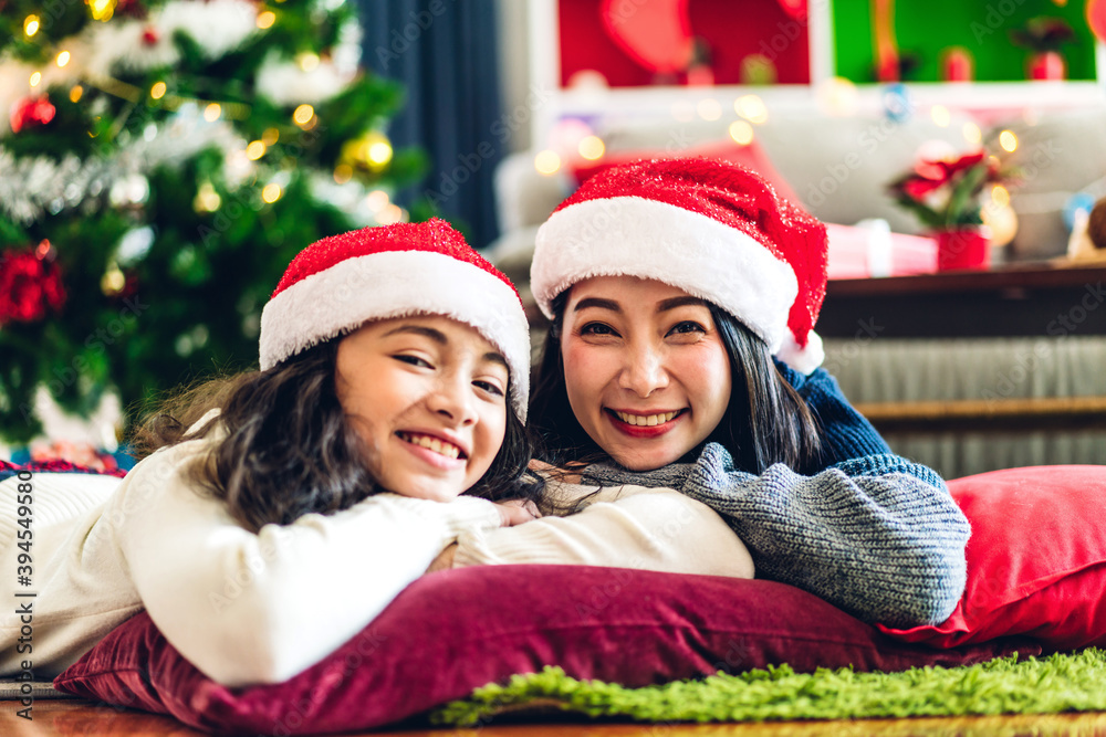 Portrait of happy asian family mother with daughter in santa hats having fun look at camera and enjoying spending time together in christmas time at home