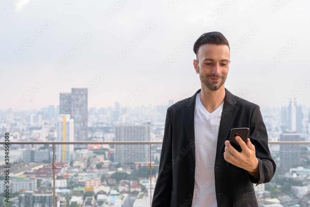 Happy businessman standing on the rooftop of a skyscraper using mobile phone Happy businessman standing on the rooftop of a skyscraper using mobile phone