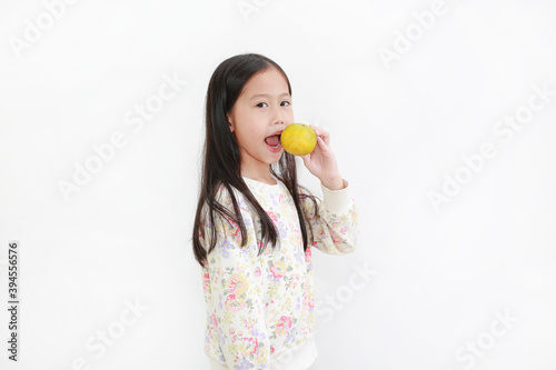 Portrait little asian kid girl holding not peeled orange fruit and gesture eating over white background