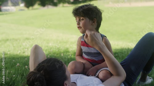 A young boy talks with his mother as he sits on her stomach while laying on a park grass