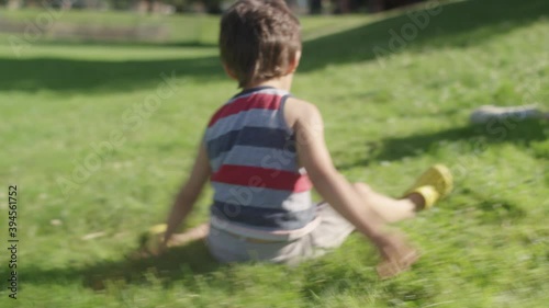 A mother and son roll down a grassy hill while playing at the park