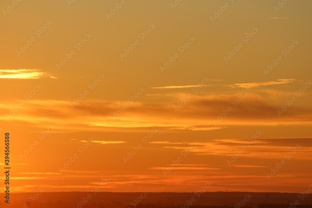 Sun below the horizon and clouds in the fiery dramatic orange sky at sunset or dawn backlit by the sun. Place for text and design Sun below the horizon and clouds in the fiery dramatic orange sky at sunset or dawn backlit by the sun. Place for text and design