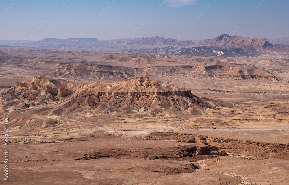 Fototapeta premium Colorful landscape of a remote desert region. Panoramic view of sandy hills, dry wadies, rock formations and boulders.