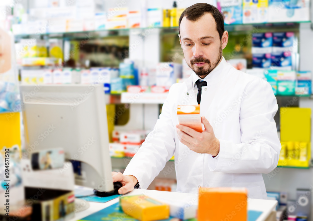 Glad male pharmacist checking assortment of drugs in pharmacy
