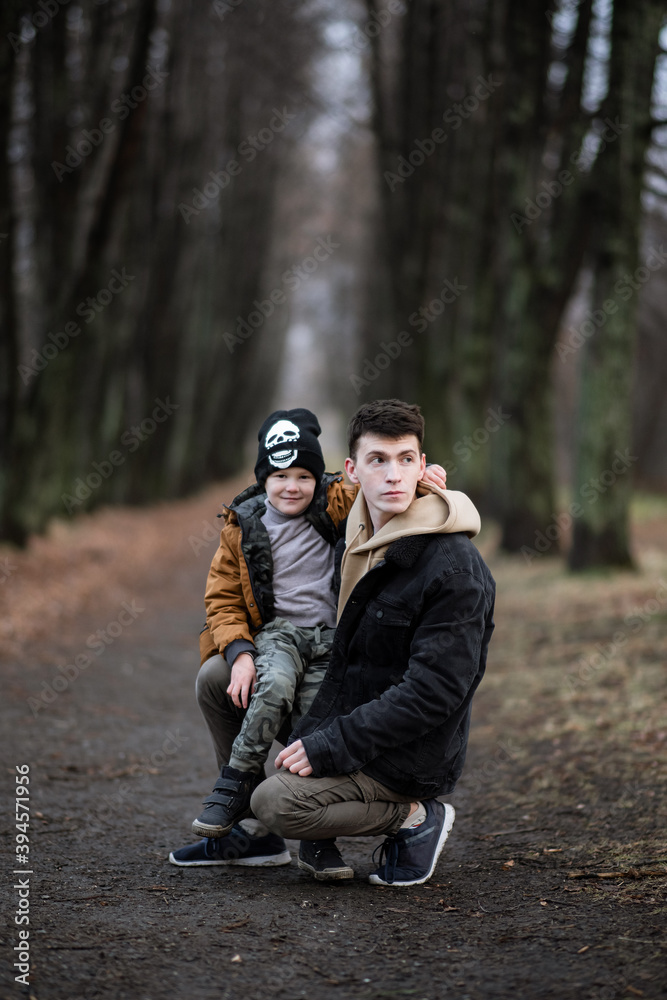 father and son are walking in the park, sitting in the middle of the alley, single father, cold spring, autumn, winter, against the background of large trees, father and dad are looking to the right