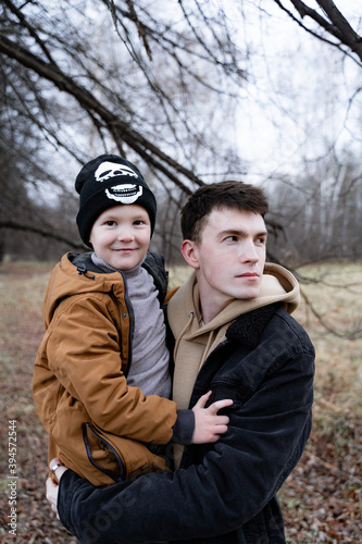 close-up portrait of a father and son, the boy smiles and the father looks to the side, the father with a pierced nose is raising a child, modern society, the son is growing up in an informal family