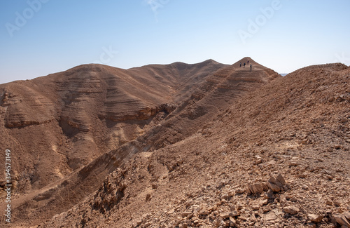 Hikers on a hiking trail in a remote desert region. Panoramic desert landscape of colorful sandy hills, dry wadies, rock formations and boulders.