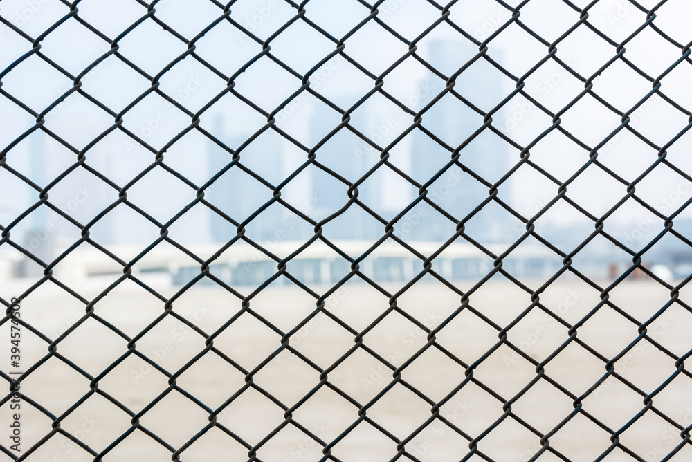 Steel wire mesh as a fence with blurred background of skylines. Steel wire mesh as a fence with blurred background of skylines.