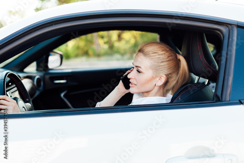 Beautiful female blonde driver talking smartphone behind the wheel of car