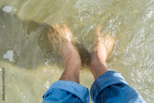 Feet of a Chinese man with jean pants, on a clear sea water in the beach of Yangxi, Yangjiang, Guangdong, China. photo