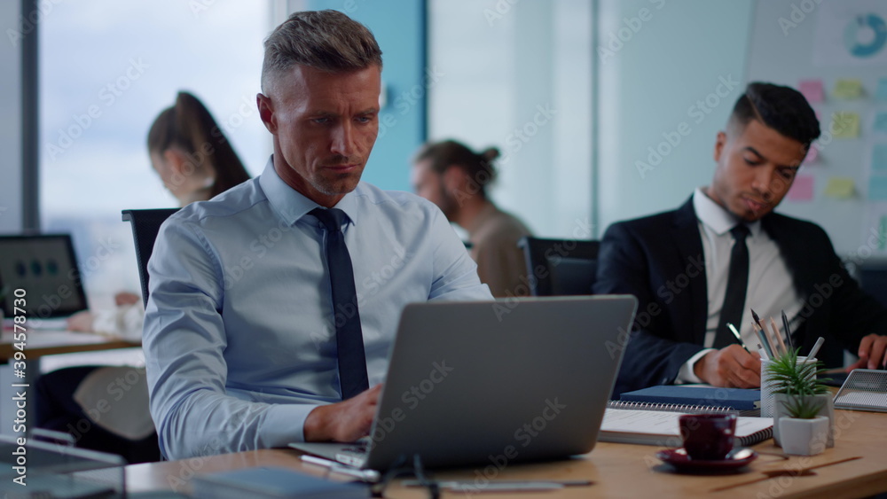 Serious businessman typing on laptop in open space. Male executive using laptop Serious businessman typing on laptop in open space. Male executive using laptop