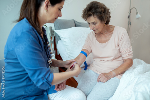 Nurse Taking Blood Samples from Senior Female Patient Sitting on Hospital Bed. Female Home Caregiver Drawing Blood From Elderly Woman.