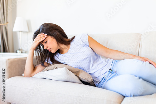 Portrait of an attractive woman lying on a sofa at home with a headache, feeling pain and with an expression of being unwell. Upset depressed woman lying on couch feeling strong headache migraine.