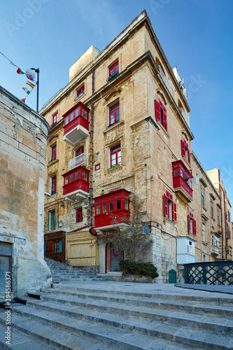 View on street of the ancient city of Valletta in evening colors. Red windows and balconies on stone palace. No people. Holidays in Malta.