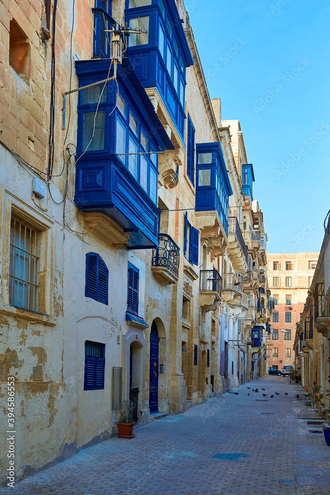 View on street of the ancient city of Valletta in evening colors. Blue windows and balconies on stone palace. No people.  Holidays in Malta.