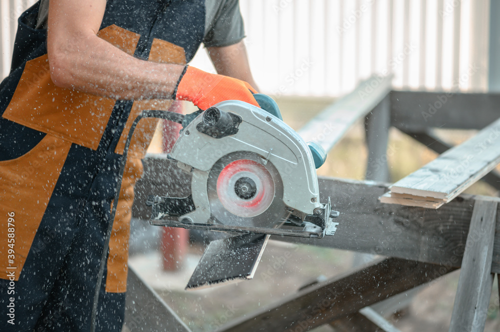 A man in uniform makes a cut of the planking Board using a circular saw. Flying sawdust, shallow depth of field. A man in uniform makes a cut of the planking Board using a circular saw. Flying sawdust, shallow depth of field.