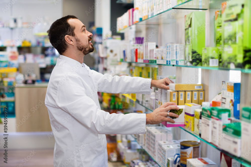 Smiling happy positive male pharmacist looking for right medicine in pharmacy