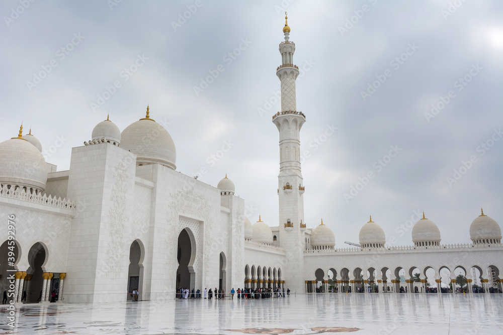 Fototapeta premium Minaret and domes of white Grand Mosque against white cloudy sky, also called Sheikh Zayed Grand Mosque, inspired by Persian, Mughal and Moorish mosque architecture