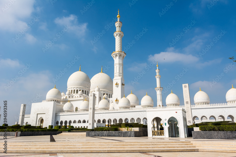 Minaret and domes of white Grand Mosque against white cloudy sky, also called Sheikh Zayed Grand Mosque, inspired by Persian, Mughal and Moorish mosque architecture