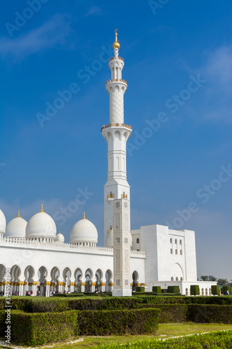 Minaret and domes of white Grand Mosque against white cloudy sky, also called Sheikh Zayed Grand Mosque, inspired by Persian, Mughal and Moorish mosque architecture