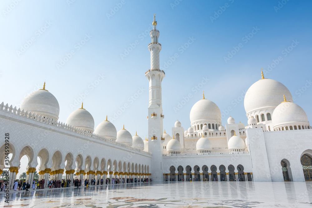 Fototapeta premium Minaret and domes of white Grand Mosque against white cloudy sky, also called Sheikh Zayed Grand Mosque, inspired by Persian, Mughal and Moorish mosque architecture