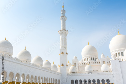 Minaret and domes of white Grand Mosque against white cloudy sky, also called Sheikh Zayed Grand Mosque, inspired by Persian, Mughal and Moorish mosque architecture