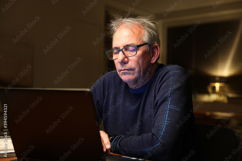 Elderly man sitting and looking on laptop, working at home, at night Elderly man sitting and looking on laptop, working at home, at night