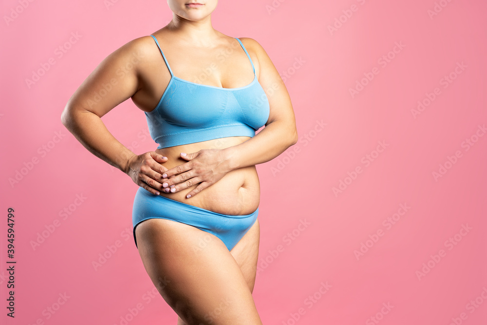 Naklejka premium Fat woman in blue underwear on pink background, overweight female body