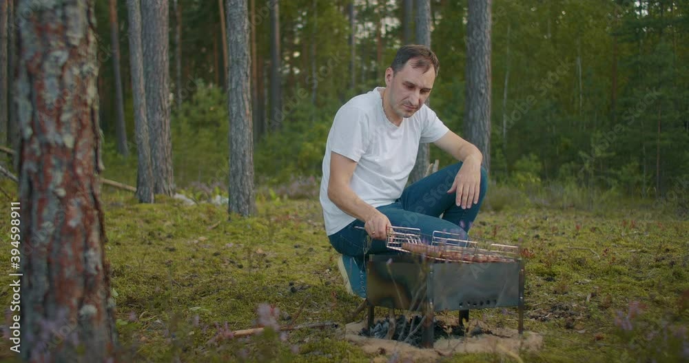 adult man is grilling sausages in forest, picnic at nature at summer weekend or vacation, resting and relax adult man is grilling sausages in forest, picnic at nature at summer weekend or vacation, resting and relax