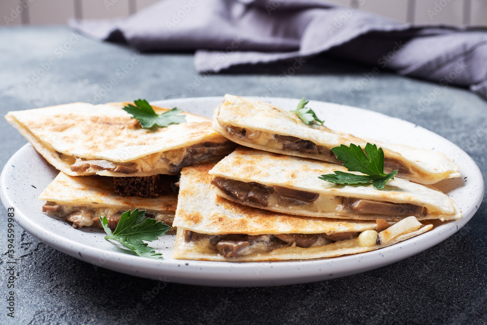 Pieces of quesadilla with mushrooms sour cream and cheese on a plate with parsley leaves. Concrete background close up.