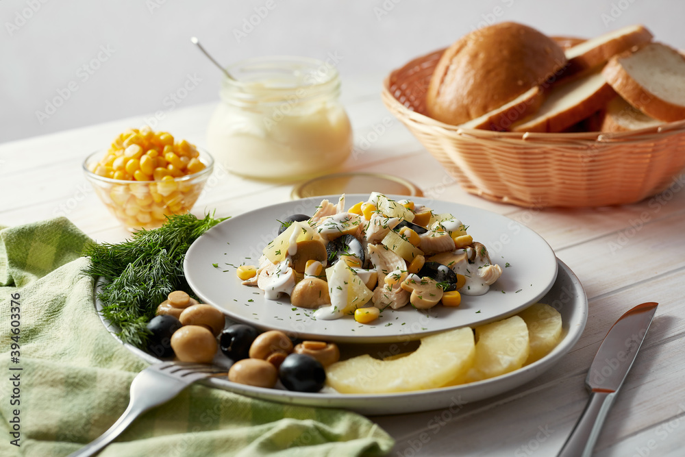 Salad with chicken, pineapple, mushrooms, olives and corn on a white plate decorated with dill