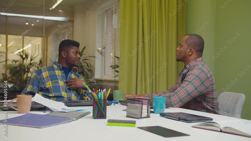 Successful handsome african male business partners in smart casual clothes sitting at office table, arguing about business matters, sharing visions and opinions while planning project in coworking. Successful handsome african male business partners in smart casual clothes sitting at office table, arguing about business matters, sharing visions and opinions while planning project in coworking.
