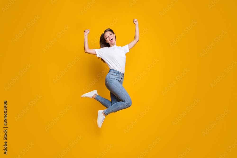 Full length body size photo of young girl fan jumping high gesturing like winner isolated on vibrant yellow color background