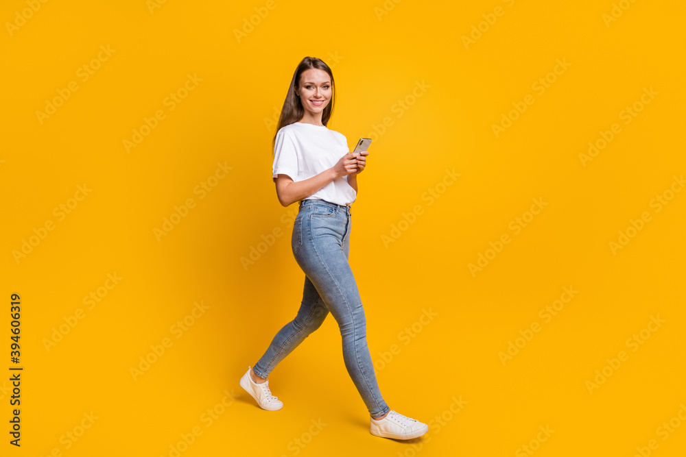 Full length body size photo of girl stepping forward using smartphone isolated on vivid yellow color background Full length body size photo of girl stepping forward using smartphone isolated on vivid yellow color background