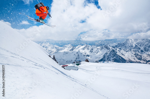 Professional athlete skier freerider in an orange suit with a backpack flies in the air after jumping on the lags on the background of blue sky and snow