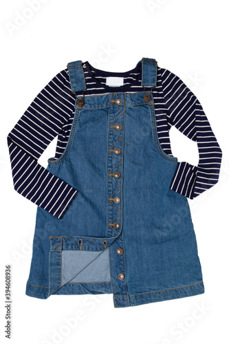 Closeup of cute sleeveless blue denim overall dress with striped t-shirt for little child girl isolated on a white background. Jeans fashion for kids.