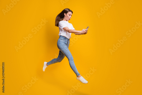 Full length body size photo of amazed female influencer jumping reading on smartphone isolated on vivid yellow color background