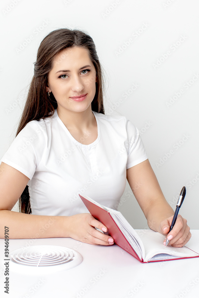 Manicure master writes notes to notebook planning her schedule at white table Manicure master writes notes to notebook planning her schedule at white table