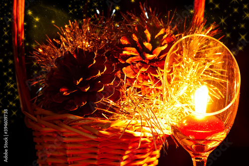 Christmas composition with goblet candle light in front of pine cones in a wicker basket on a black background .