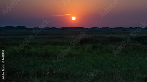 Panoramic view over the grassland between the dike and the beach against the deep setting sun on the North Sea coast. © Ralph